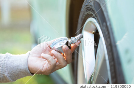 Car owner uses a pressure gauge to check tire inflation, emphasizing vehicle readiness and the importance of proper tire maintenance before embarking on a journey Car owner uses a pressure gauge to check tire inflation, emphasizing vehicle readiness and the importance of proper tire maintenance before embarking on a journey 119800090