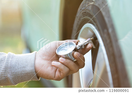 Car owner uses a pressure gauge to check tire inflation, emphasizing vehicle readiness and the importance of proper tire maintenance before embarking on a journey 119800091