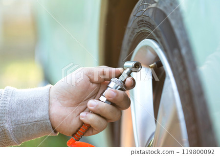 Car owner inflates a tire, highlighting the importance of tire maintenance and pressure checks to ensure safe, smooth travel and readiness before a journey Car owner inflates a tire, highlighting the importance of tire maintenance and pressure checks to ensure safe, smooth travel and readiness before a journey 119800092