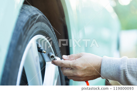 Car owner inflates a tire, highlighting the importance of tire maintenance and pressure checks to ensure safe, smooth travel and readiness before a journey 119800093