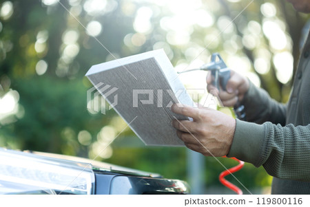 Car owner holds an air filter for examination. Importance of regular inspection, cleaning, and replacement of car air filters, Emphasizes maintenance for better air quality and vehicle efficiency Car owner holds an air filter for examination. Importance of regular inspection, cleaning, and replacement of car air filters, Emphasizes maintenance for better air quality and vehicle efficiency 119800116
