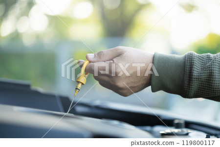 Car owner pulls out the dipstick to check engine oil levels, highlighting the importance of regular oil maintenance for optimal engine performance and vehicle longevity 119800117