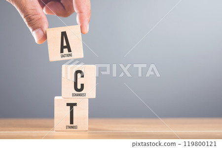 A hand arranging wooden blocks with the letters A, C and T on a table, set against a gray. Symbolizes the process of taking action to implement changes in various aspects of life or business 119800121
