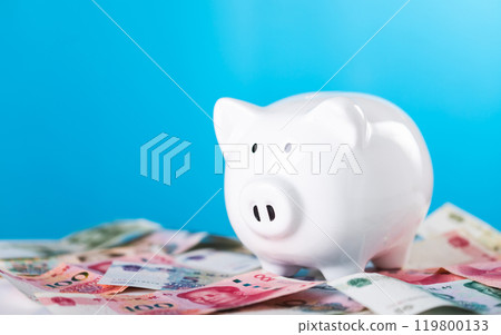 White piggy bank and Chinese Yuan currency placed on a table, set against a light blue background. The image symbolizes savings and financial management with a focus on China's economy White piggy bank and Chinese Yuan currency placed on a table, set against a light blue background. The image symbolizes savings and financial management with a focus on China's economy 119800133