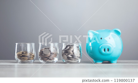 Man dropping coins into a glass jar, with a piggy bank nearby. Represents the concept of saving money, highlighting the importance of building a financial cushion through various saving methods. 119800137