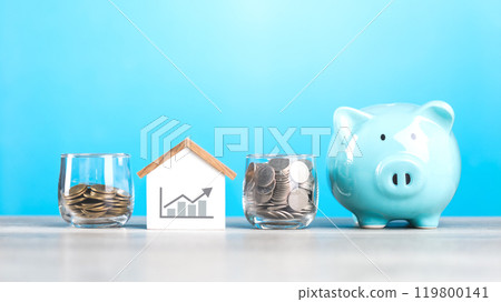 Man drops coins into a glass jar, with piggy bank and a wooden house model beside him. Emphasizes the concept of saving money for future house investments and financial stability 119800141