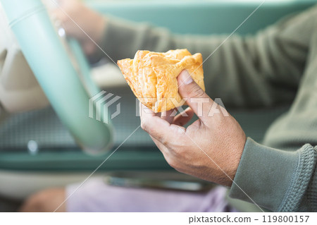 Car owner enjoys a pie while seated inside. Highlighting the impact of food scents in car interiors, Reflects the experience of eating on the go and its effect on cabin air quality 119800157