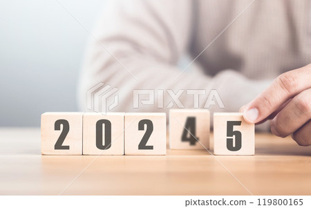 Hand replaces "2024" with "2025" using number blocks, symbolizing the transition into the new year, representing change, progress, and the ongoing passage of time Hand replaces "2024" with "2025" using number blocks, symbolizing the transition into the new year, representing change, progress, and the ongoing passage of time 119800165