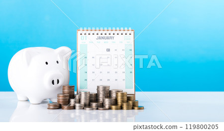A stack of coins, a piggy bank, and a 2025 desk calendar placed together. Represents financial planning for the upcoming year, emphasizing the importance of saving and managing money effectively 119800205