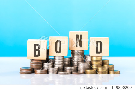 Stack of various types coins alongside a wooden block labeled BOND. Steady and structured growth linked to bond investments, highlighting stability and the importance of long-term financial planning 119800209