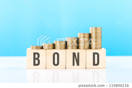 Stack of various types coins alongside a wooden block labeled BOND. Steady and structured growth linked to bond investments, highlighting stability and the importance of long-term financial planning 119800216