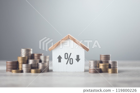 Stacks of coins arranged from smallest to largest, alongside a wooden house model on a table against a grey background. Concept of saving money for future investments, particularly in real estate Stacks of coins arranged from smallest to largest, alongside a wooden house model on a table against a grey background. Concept of saving money for future investments, particularly in real estate 119800226