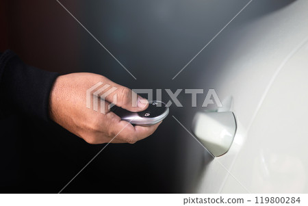 A man's hand holding a car remote to unlock the vehicle. The image represents the concept of using a car remote, highlighting the role of remote battery power in accessing and securing the car 119800284