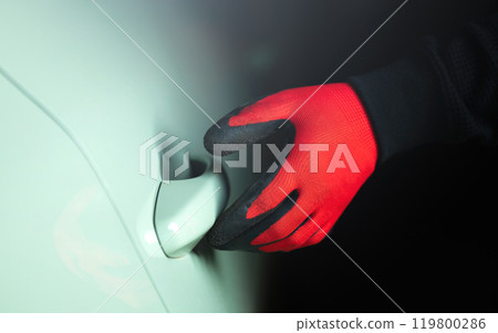 Man's gloved hand holding a screwdriver, attempting to pry open a car door handle. The image represents the concept of car theft, highlighting the risk and importance of vehicle security 119800286