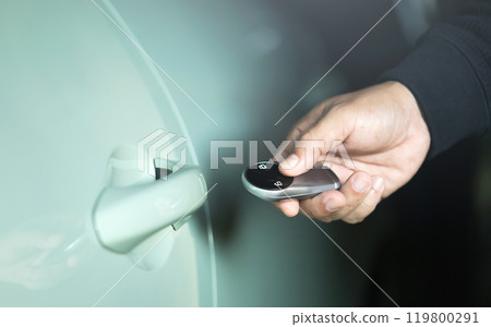 A man's hand holding a car remote to unlock the vehicle. The image represents the concept of using a car remote, highlighting the role of remote battery power in accessing and securing the car A man's hand holding a car remote to unlock the vehicle. The image represents the concept of using a car remote, highlighting the role of remote battery power in accessing and securing the car 119800291
