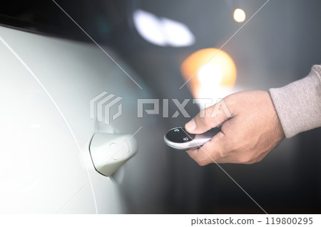 A man's hand holding a car remote to unlock the vehicle. The image represents the concept of using a car remote, highlighting the role of remote battery power in accessing and securing the car 119800295