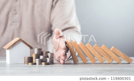 Businessman uses his hand to stop wooden blocks from falling, symbolizing the protection of assets and strategic decision-making in managing resources effectively, domino effect and risk management 119800301