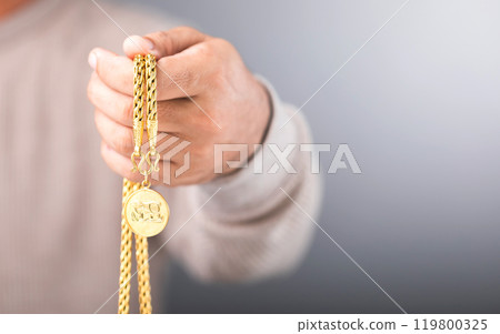 A close-up of a man holding a gold necklace in his hand, symbolizing the concept of gold market value. Reflects checking the authenticity of the gold, exploring whether it's genuine or counterfeit 119800325