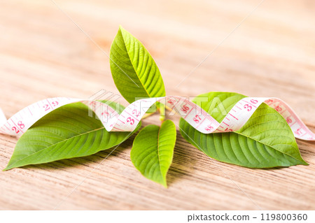 A green kratom leaf next to a measuring tape, symbolizing the misconception that consuming kratom aids in weight loss. Reflects discussions about kratom's effects on health and dietary habits A green kratom leaf next to a measuring tape, symbolizing the misconception that consuming kratom aids in weight loss. Reflects discussions about kratom's effects on health and dietary habits 119800360