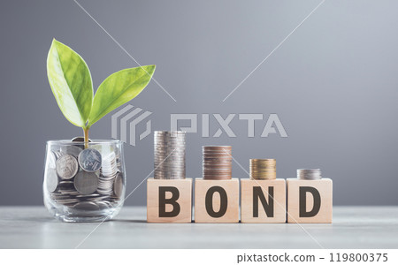 A hand stacking coins on a wooden block labeled 'BOND,' The image reflects the steady and structured growth associated with bond investments, emphasizing stability and financial planning 119800375