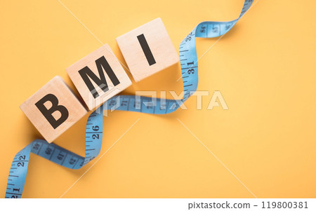 Wooden block displaying 'BMI' next to a measuring tape on yellow background. The concept of Body Mass Index, highlighting the importance of health metrics in tracking fitness and well-being 119800381