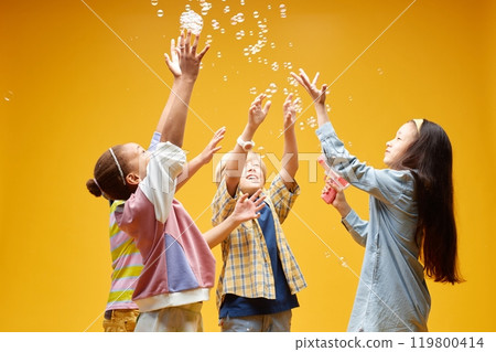 Candid shot of diverse group of four little kids standing in circle catching floating soap bubbles against orange background in studio, copy space Candid shot of diverse group of four little kids standing in circle catching floating soap bubbles against orange background in studio, copy space 119800414
