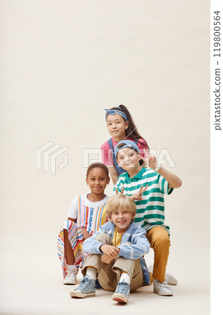 Vertical full shot of diverse group of four positive kids in colorful clothes having fun posing for camera together while showing V sign and smiling against neutral background in studio, copy space Vertical full shot of diverse group of four positive kids in colorful clothes having fun posing for camera together while showing V sign and smiling against neutral background in studio, copy space 119800564