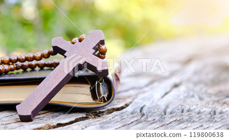 Dark red wooden cross leaning against an old open book symbolizing the spread of Jesus Christs love among Christians reflecting faith devotion and the importance of Christian teachings. Dark red wooden cross leaning against an old open book symbolizing the spread of Jesus Christs love among Christians reflecting faith devotion and the importance of Christian teachings. 119800638