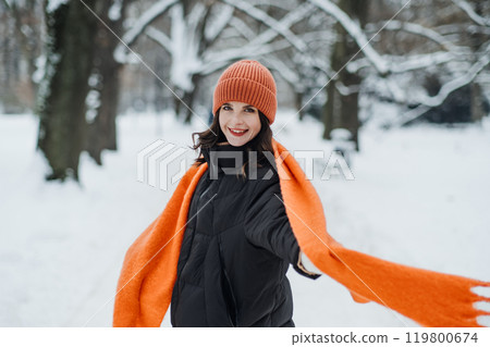 Woman in orange scarf and hat enjoying a snowy walk. Bold winter accessories, vibrant fashion, and colorful layering. 119800674
