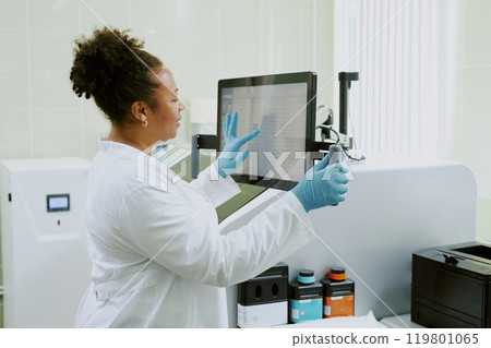 Medical professional interacting with a large touchscreen monitor in a brightly lit clinical environment, wearing lab coat and gloves, absorbed in work 119801065