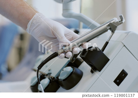 Gloved hand handling medical equipment in a sterile surgery room environment. Close-up shot showcasing precision and focus during delicate operation preparations Gloved hand handling medical equipment in a sterile surgery room environment. Close-up shot showcasing precision and focus during delicate operation preparations 119801137