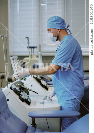 Healthcare professional focusing on modern medical equipment in a clinical setting. Engaging with advanced devices for patient care and support 119801140