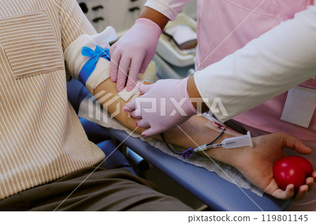 Medical professional administering injection using gloves on patient's arm with blue tourniquet applied in clinical setting Medical professional administering injection using gloves on patient's arm with blue tourniquet applied in clinical setting 119801145