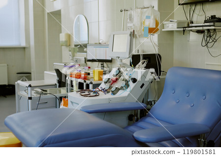Medical room displaying high-tech equipment, medical supplies, and comfortable seating at a hospital. Room is well-lit with organized, clean surfaces and several devices present 119801581