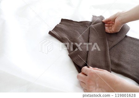 A woman's hands folding a simple brown knitted garment A woman's hands folding a simple brown knitted garment 119801628