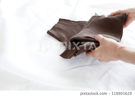 A woman's hands folding a simple brown knitted garment A woman's hands folding a simple brown knitted garment 119801629