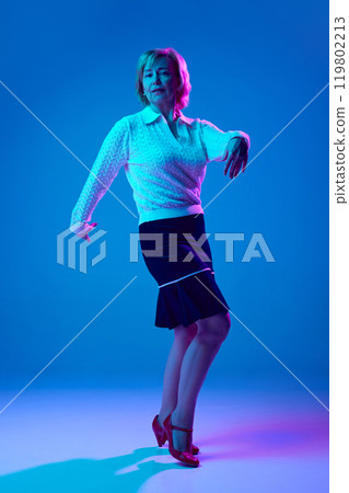 Full-length portrait of elegant elderly woman dancing, posing against blue studio background in neon light 119802213