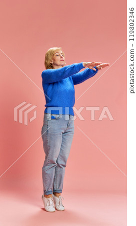Checking health condition. Full-length of mature, elderly woman in casual wear, showing balance of body against pink studio background 119802346