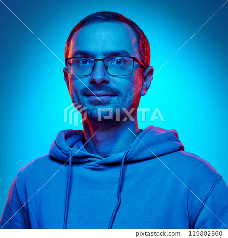 Close-up photo of young attractive man with glasses looking at camera in neon light against gradient studio background. Close-up photo of young attractive man with glasses looking at camera in neon light against gradient studio background. 119802860