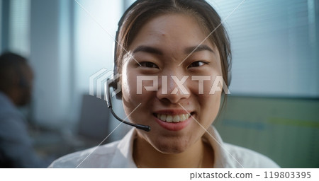 Female hotline operator in headset smiles and looks at camera 119803395