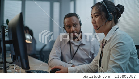 Two diverse technical support specialists wearing headsets talking with client 119803398