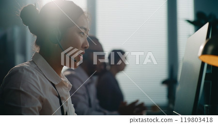 Close up of Asian helpline operator in headset having conversation on call Close up of Asian helpline operator in headset having conversation on call 119803418