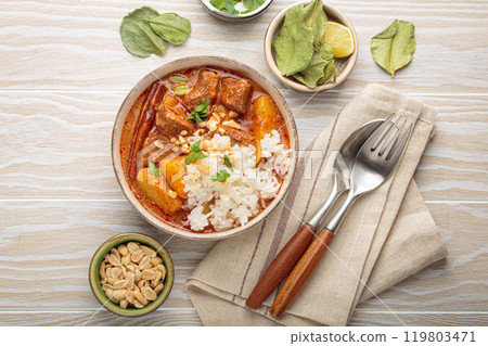 Delicious massaman curry with beef, potatoes, rice, and peanuts on white wooden background, traditional thai cuisine 119803471