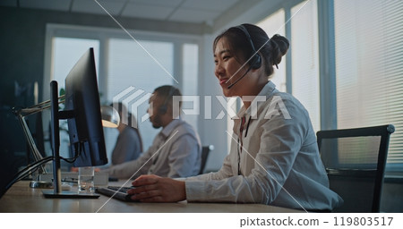 Stressed Asian hotline operator finishing phone call, holding head Stressed Asian hotline operator finishing phone call, holding head 119803517