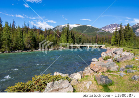A cement bridge over a river in forest against blue sky and a mountain in the background. Maligne River in Jasper National Park, Alberta, Canada. Canadian Rockies. 119803873
