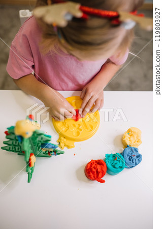 Child engaged in creative play with colorful modeling clay at a table in a bright indoor space 119803927