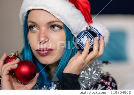 Portrait of a beautiful caucasian hipster woman in Christmas clothes. Posing looking sideways holding colorful balls and a silver decoration around her neck. Beauty, Christmas holidays, positivity Portrait of a beautiful caucasian hipster woman in Christmas clothes. Posing looking sideways holding colorful balls and a silver decoration around her neck. Beauty, Christmas holidays, positivity 119804968