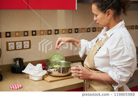 Woman seasoning food in a modern kitchen setting Woman seasoning food in a modern kitchen setting 119805988