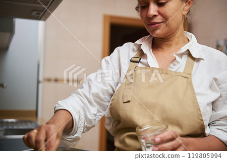 Woman cooking in kitchen wearing apron and preparing a meal 119805994