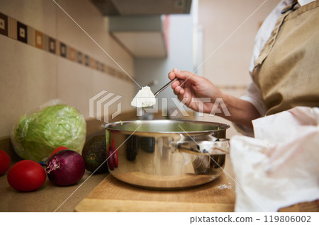 Home cooking: adding ingredients to a pot on a kitchen counter 119806002